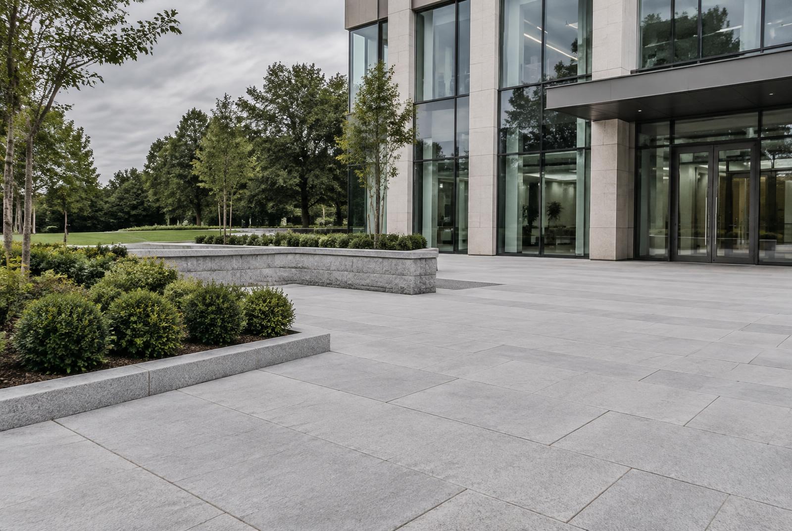 New granite-paved office entrance with crisp joints, kerb edging, a low stone wall and tidy planting