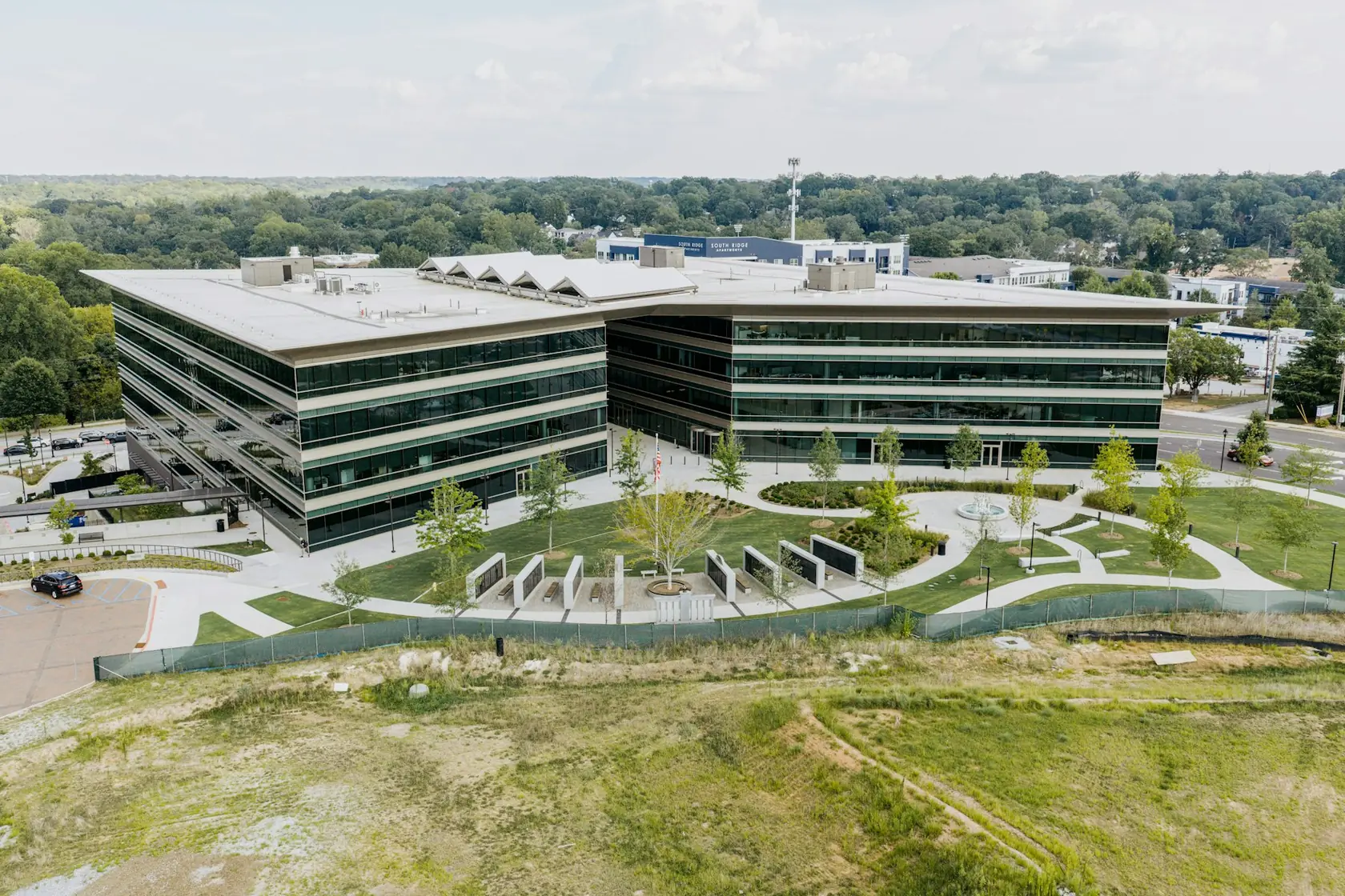A landscaped plaza with stone walls and walkways in front of a curved glass office building, with grass and trees around